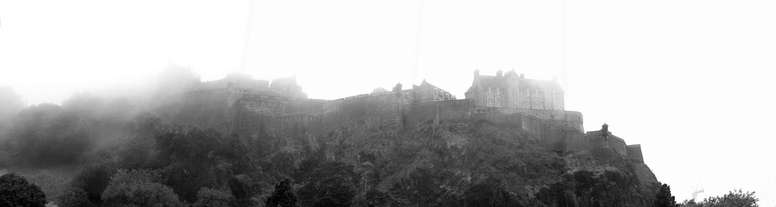 Dramatic monochrome panorama of Edinburgh Castle shrouded in thick morning mist on its rocky crag.